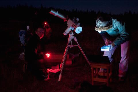 Participants hunched over operating a telescope at night.